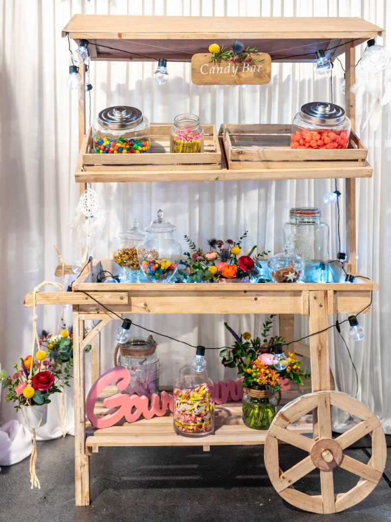 Candy bar coloré sur chariot en bois avec bonbons variés et décorations florales.