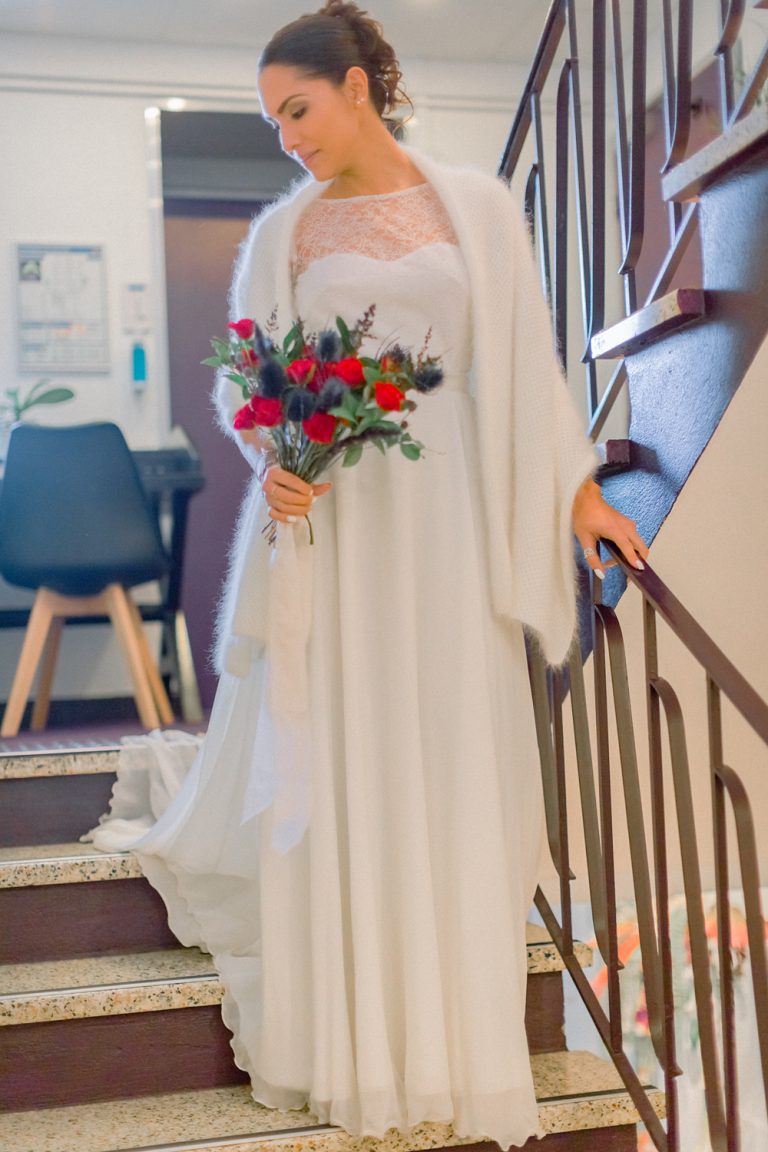 Mariée qui descend les escaliers avec une robe blanche et un bouquet rouge