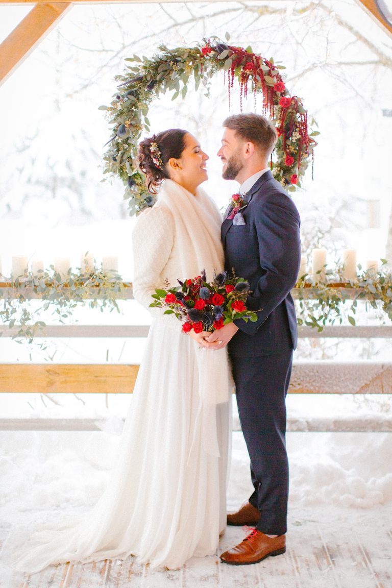 Mariés qui se regardent dans la neige avec un bouquet rouge dans la main
