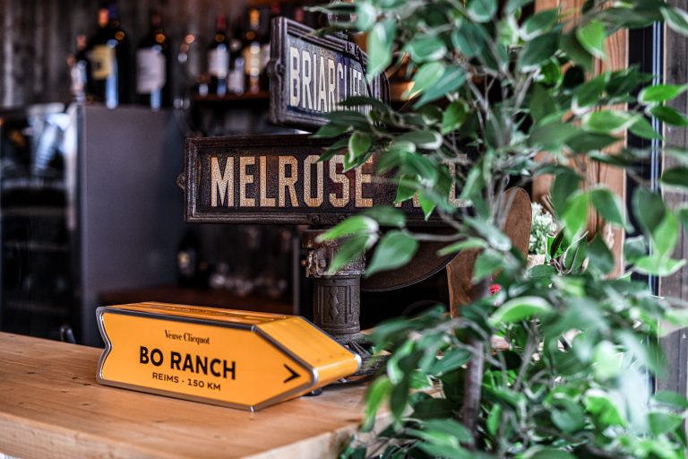 Enseignes vintage "Melrose" et flèche "Bo Ranch" dans un décor de bar avec plantes.