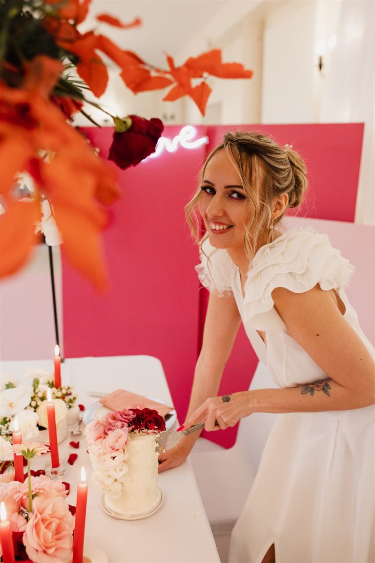 Mariée qui découpe le gateau de mariage blanc et rouge passion