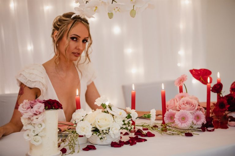 Mariée à la table de shooting mariage décoré avec bougie et fleur blanches et rouges