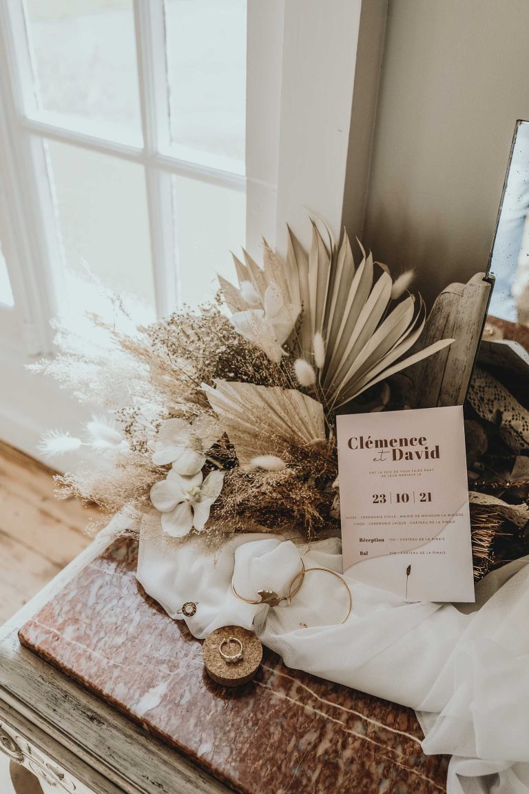 Arrangement floral délicat avec invitation de mariage pour Clémence et David, alliances sur tissu élégant, sur une table vintage