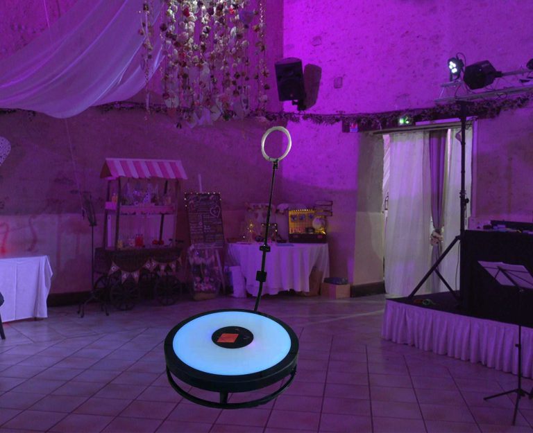 Salle de réception de mariage éclairée en violet avec piste de danse, DJ booth, et chariot de bonbons.