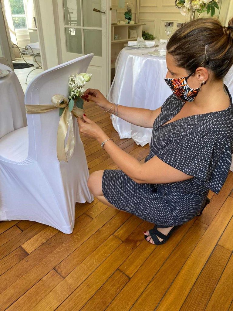 Une organisatrice de mariage attache des fleurs à une chaise blanche dans une salle élégante.