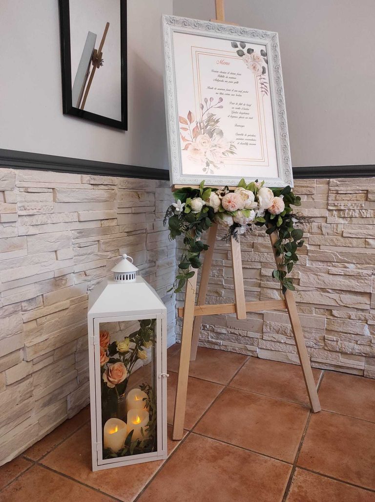 Grand menu de mariage affiché sur un chevalet, entouré de fleurs et de bougies.