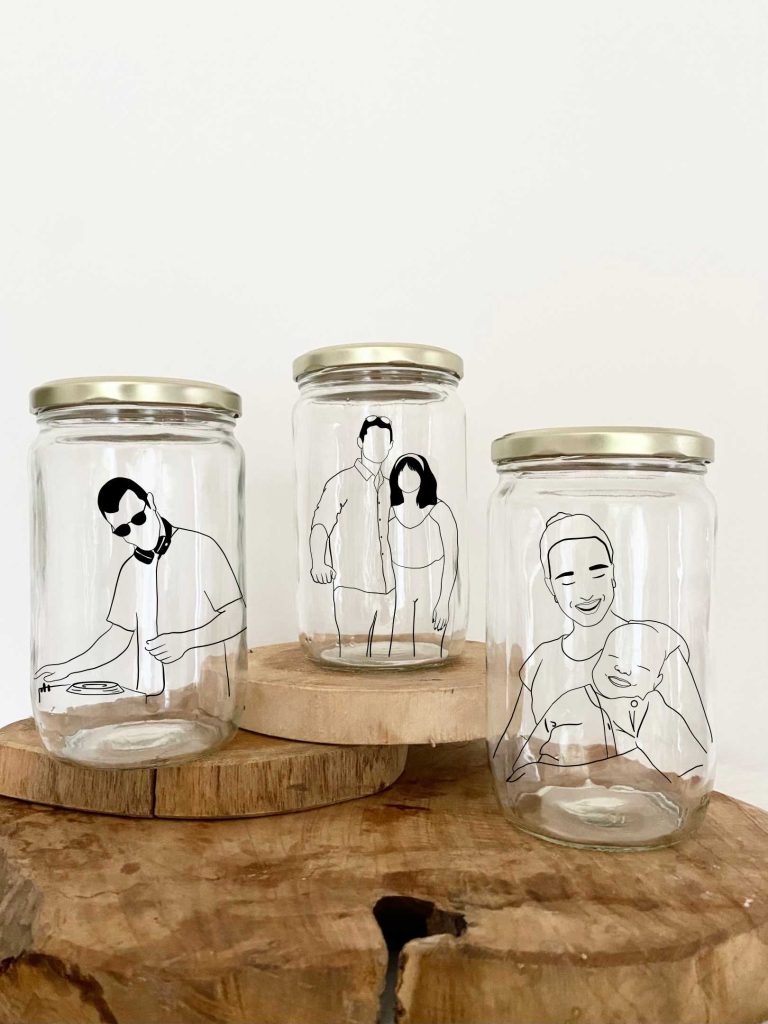 Trois bocaux en verre avec des illustrations personnalisées sur bois brut.