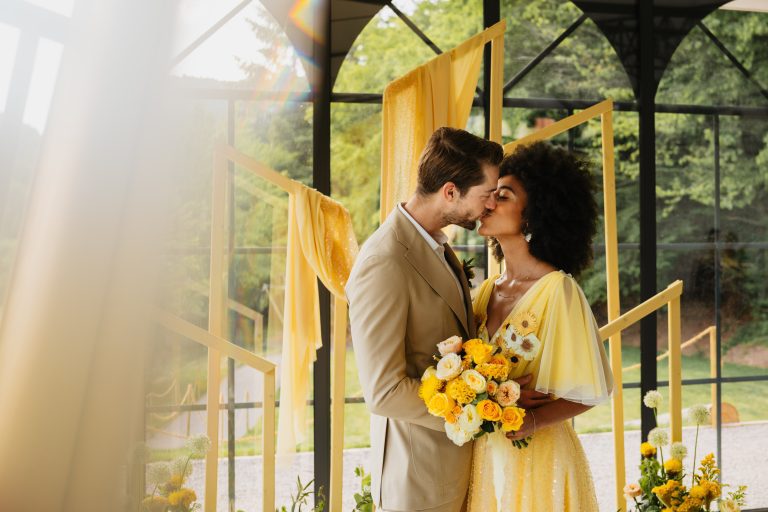 couple qui s'embrassent avec la femme qui porte une robe jaune et tiens sobnt bouquet et le maris qui porte un costume