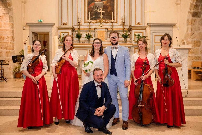 Quatuor à cordes féminin en robes rouges posant avec les mariés dans une église.