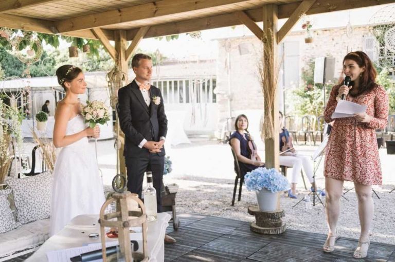 Mariée et marié écoutant attentivement leur amie leur adressant un discours lors de la cérémonie en plein air.