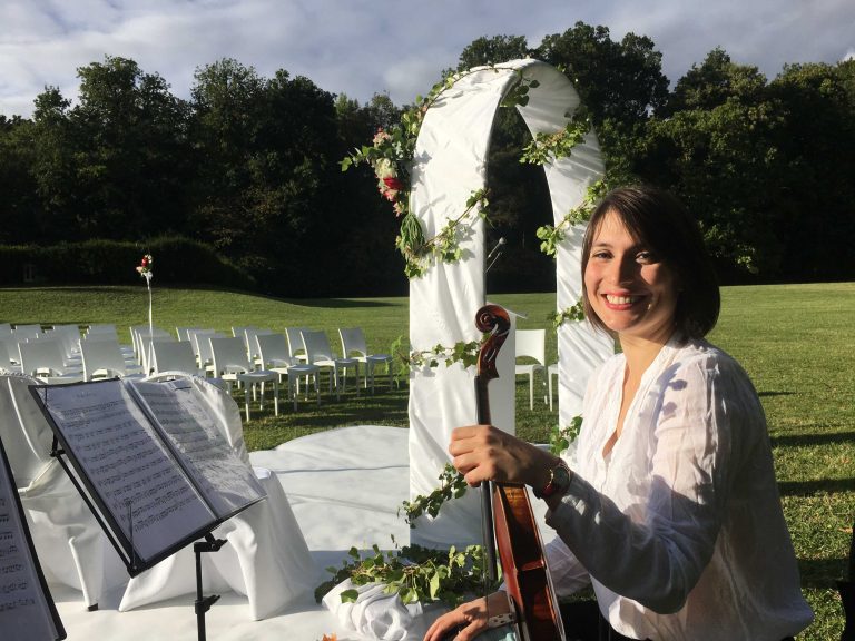 Alice, souriante, tenant son violon à une cérémonie de mariage en plein air, prête à remplir l'air de mélodies enchanteresses.