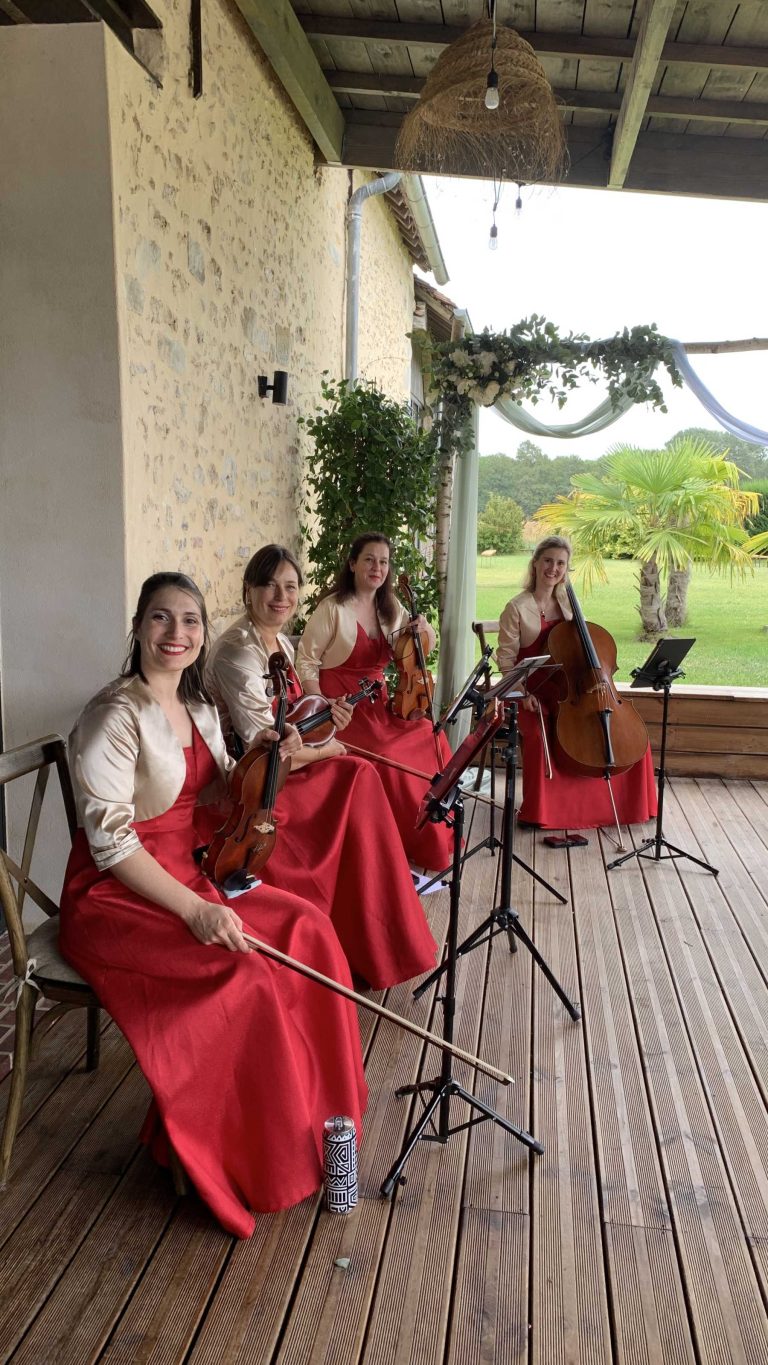 Quatuor à cordes féminin jouant à un mariage en plein air sur une terrasse en bois.