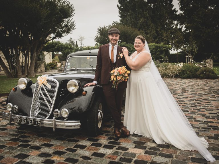 Jeunes mariés en robe et costume avec une Citroën à l'arrière