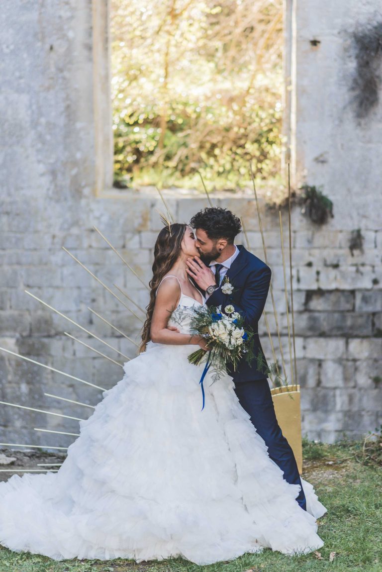 Jeunes mariés s'embrassant tendrement, la mariée tenant un bouquet et le marié en costume bleu.