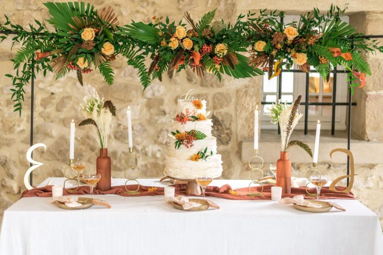 Table de gâteau de mariage avec décoration florale luxuriante et bougies sur fond de mur en pierre.