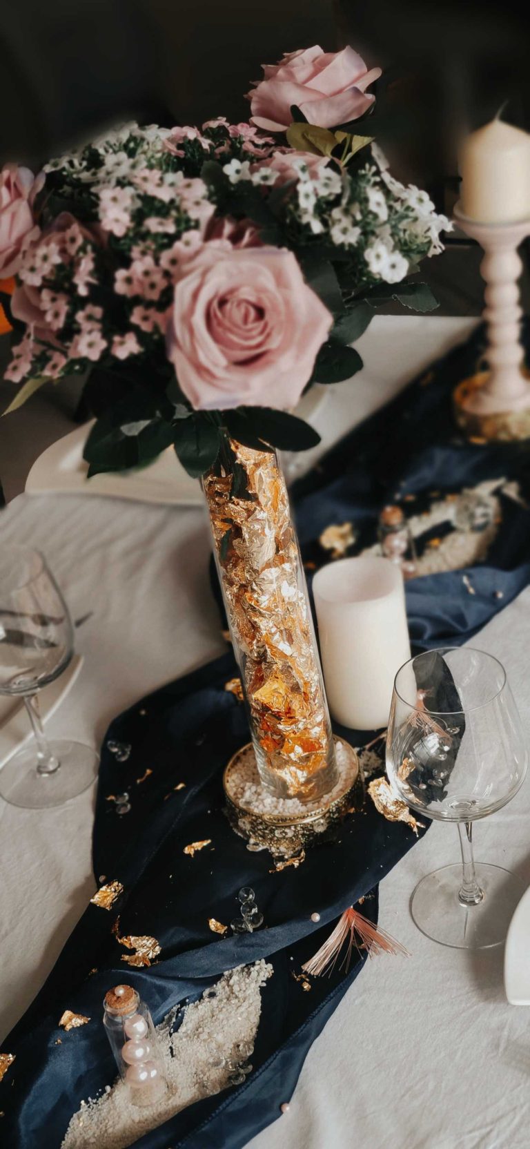Décoration de table de mariage avec bouquets de roses, bougies et accents dorés sur nappe bleu nuit.