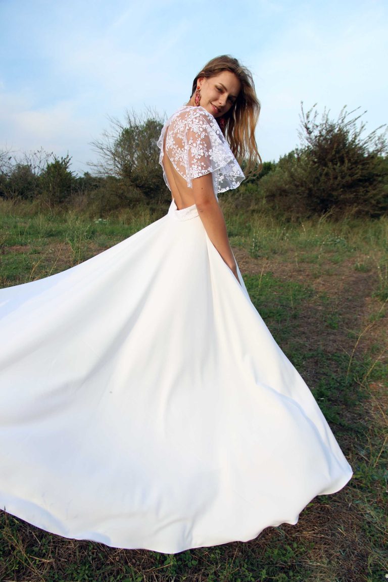 Mariée souriante en robe de satin avec cape en dentelle dans un champ.