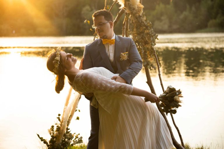 Mariée échangeant des voeux avec son mari au coucher du soleil au bord d'un lac