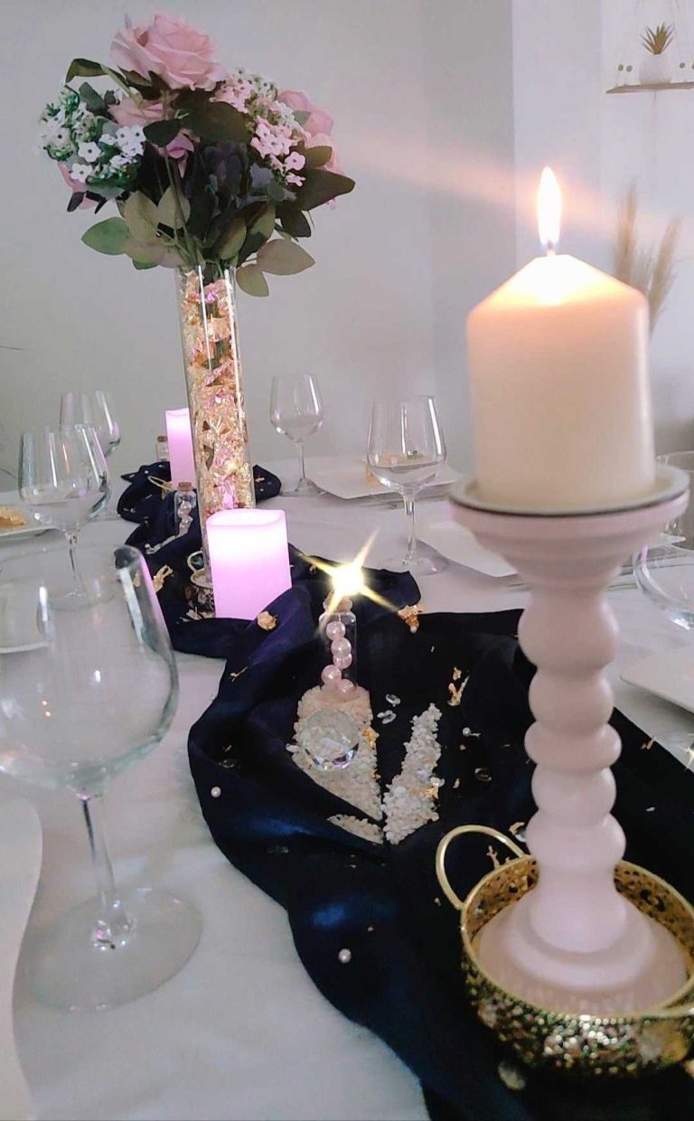 Table de mariage décorée avec des roses, bougies et un chemin de table bleu avec des éclats dorés.