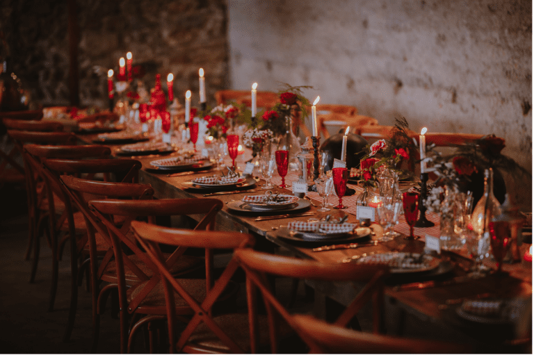 Longue table de mariage décorée en rouge et or sous un éclairage intime.