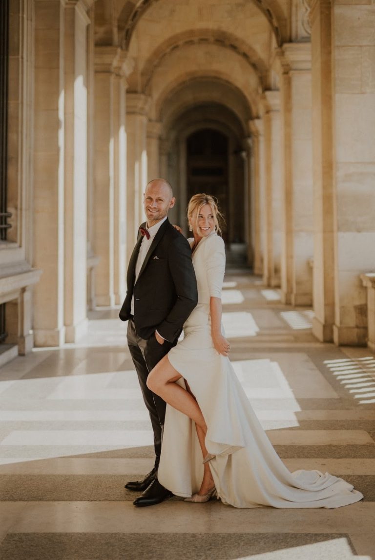 Couple de mariés posant dans un couloir architectural majestueux.