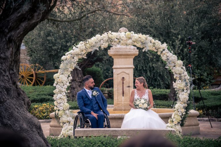 Couple de mariés échangeant des vœux, marié en fauteuil roulant sous un arc floral