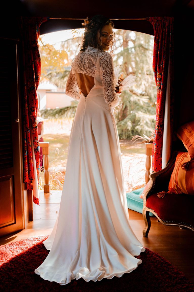 Mariée en robe bohème regardant par la fenêtre de la roulotte.