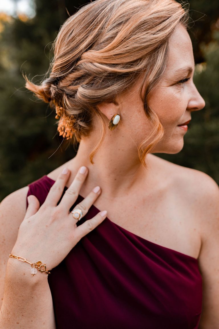 Femme portant une robe bordeaux avec des bijoux élégants, dont une boucle d'oreille, un bracelet et une bague.