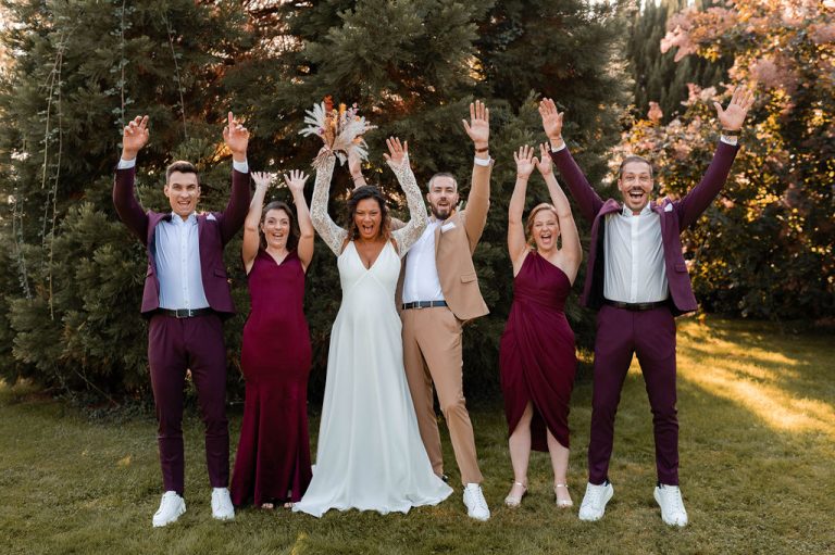 Groupe joyeux de mariés et invités levant les mains en l'air dans un jardin.
