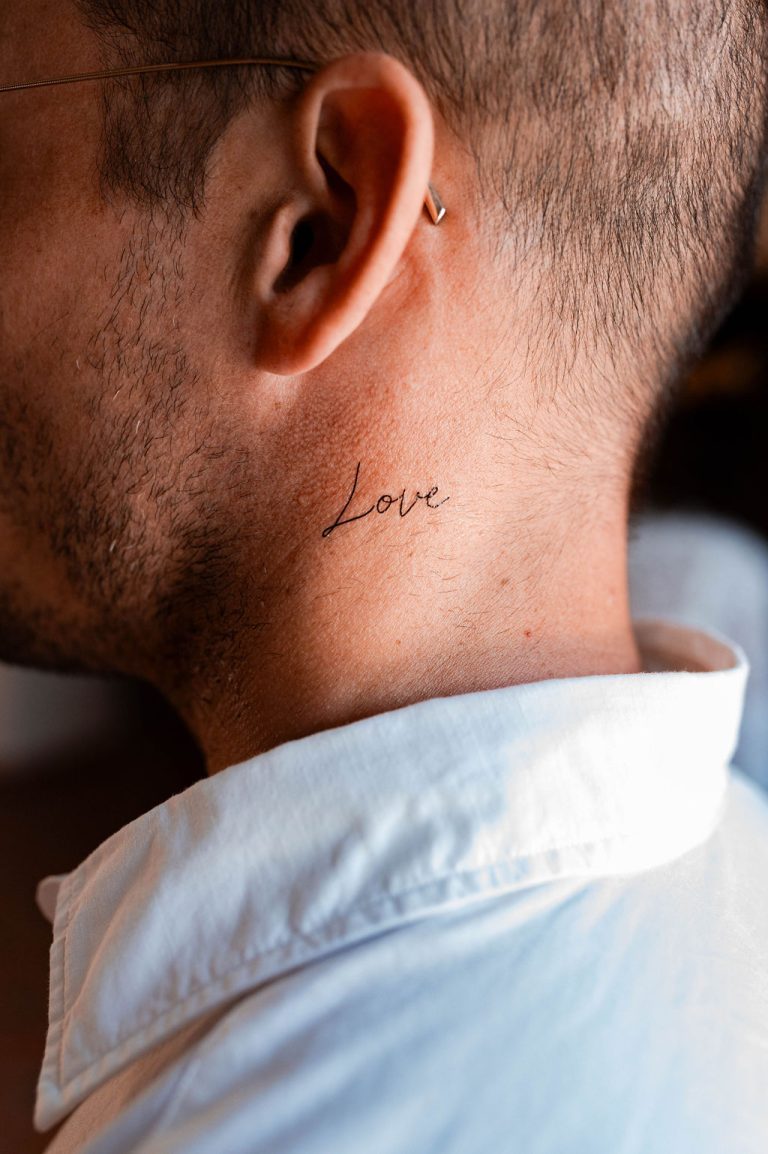 Homme de profil avec un tatouage temporaire "Love" écrit derrière l'oreille.