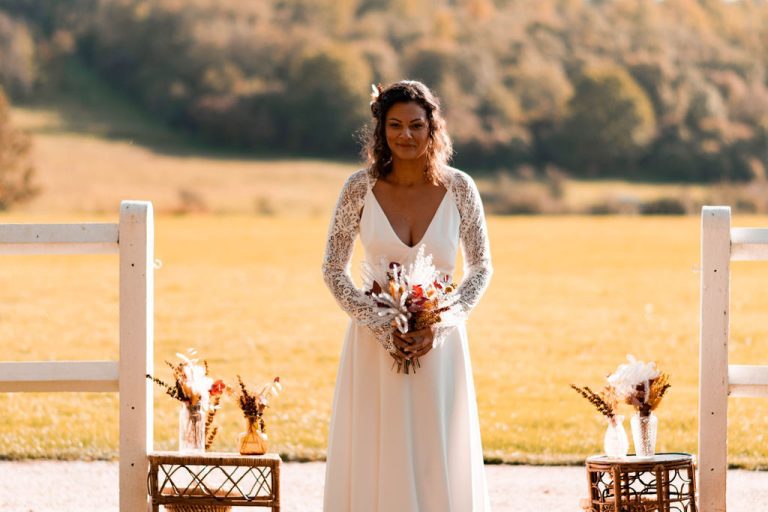 Mariée tenant un bouquet gypsy bohème devant un paysage champêtre.