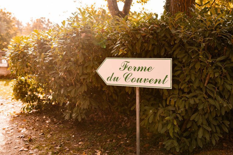 Panneau "Ferme du Couvent" devant un buisson, éclairé par la lumière dorée du soleil.