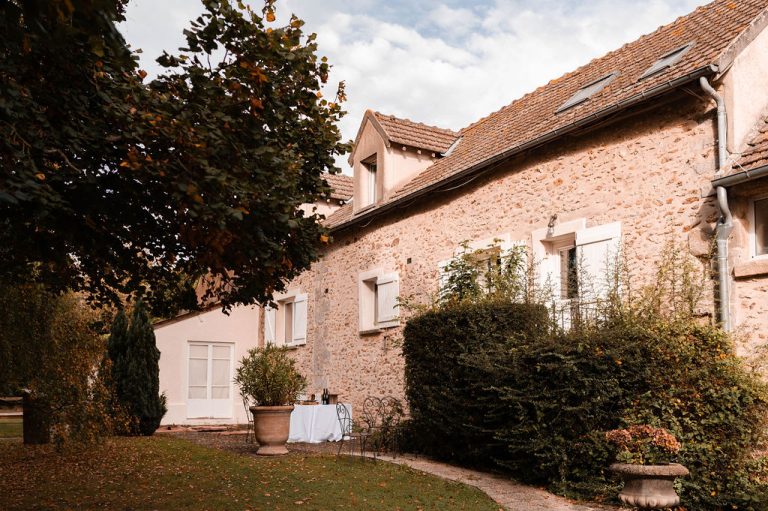 Vue extérieure d'une maison de campagne avec des arbres aux feuilles verdoyantes.