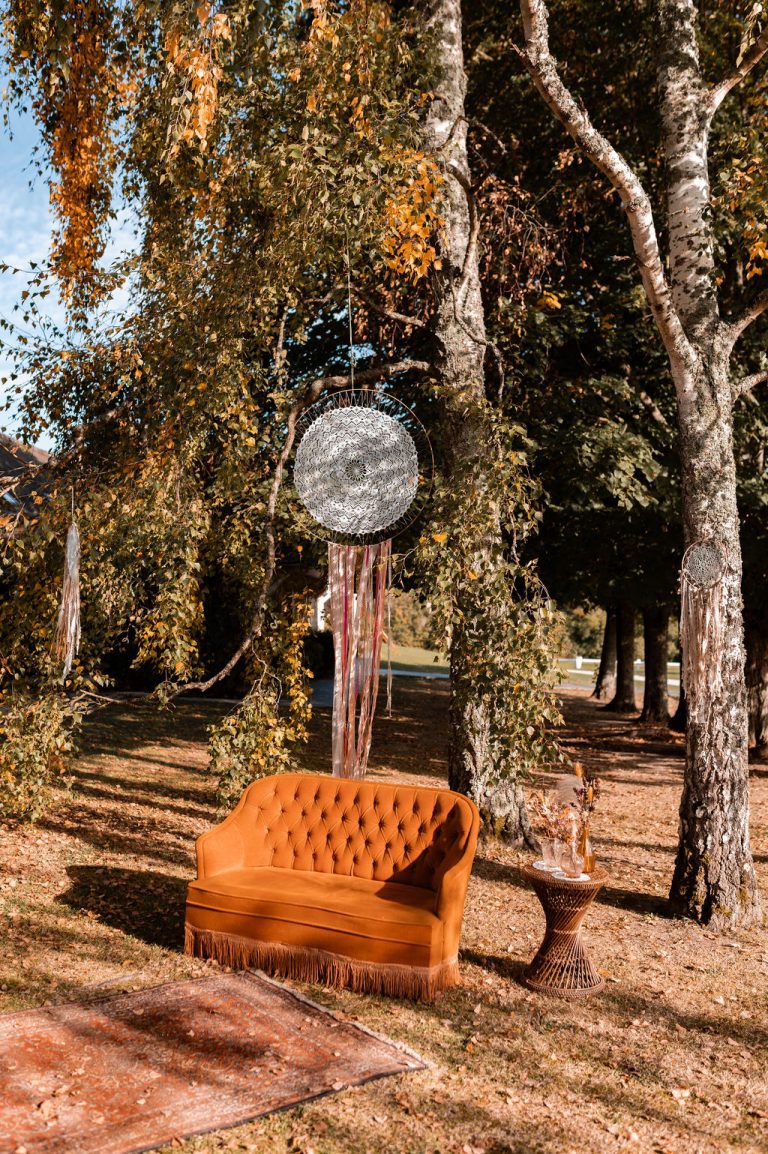 Un coin détente bohème à l'extérieur avec un canapé orange et des décorations suspendues.