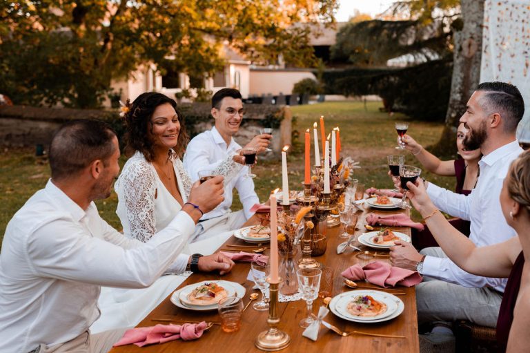 Groupe d'amis et famille partageant un repas autour d'une table décorée dans un style bohème en extérieur.
