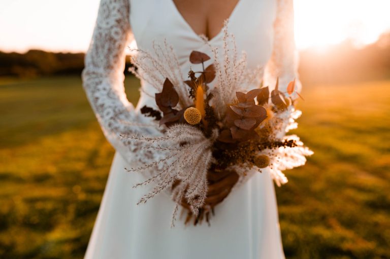 Mariée tenant un bouquet bohème avec des fleurs séchées au coucher du soleil.