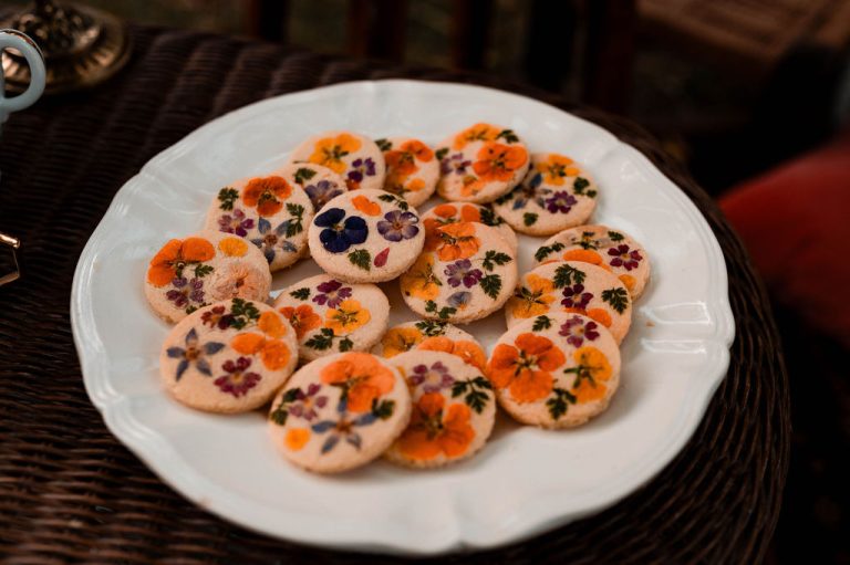 Assiette de biscuits décorés de fleurs comestibles sur une table en rotin.