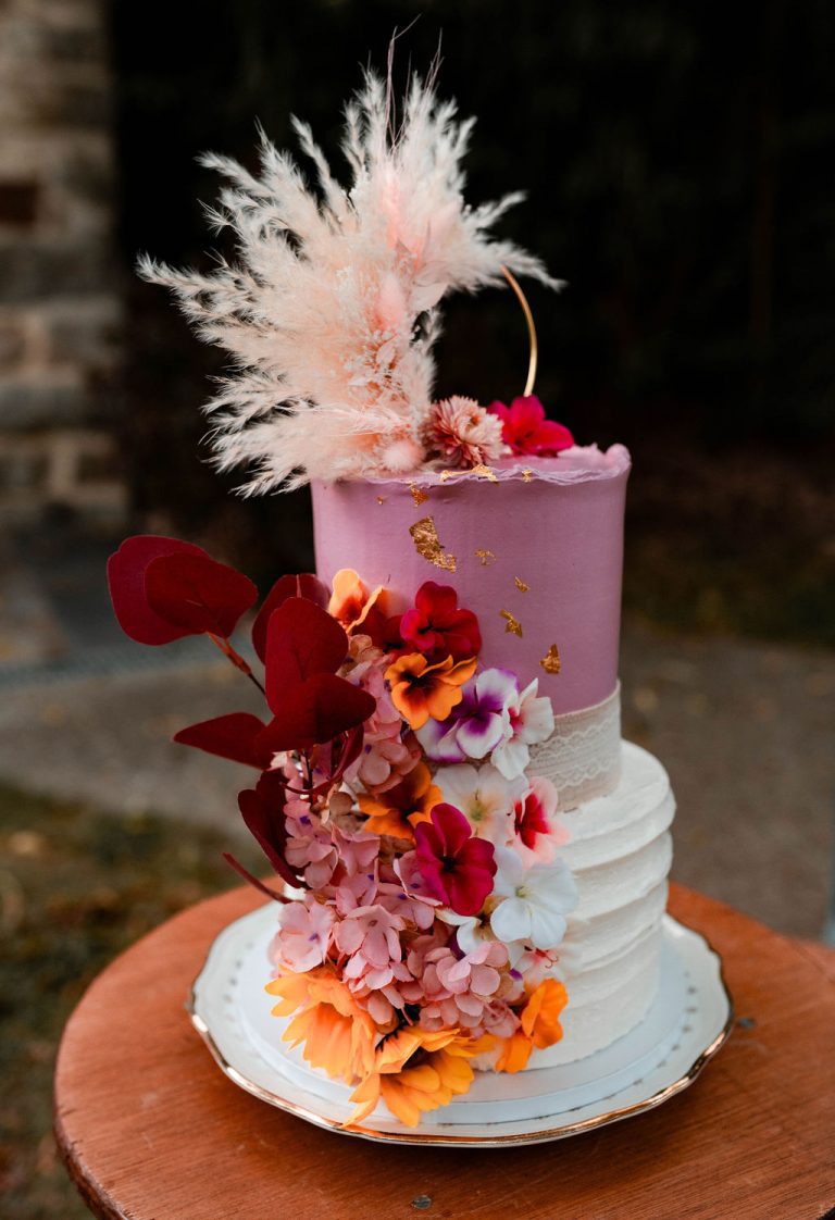 Gâteau de mariage à étages décoré de fleurs et de plumes sur un fond naturel.