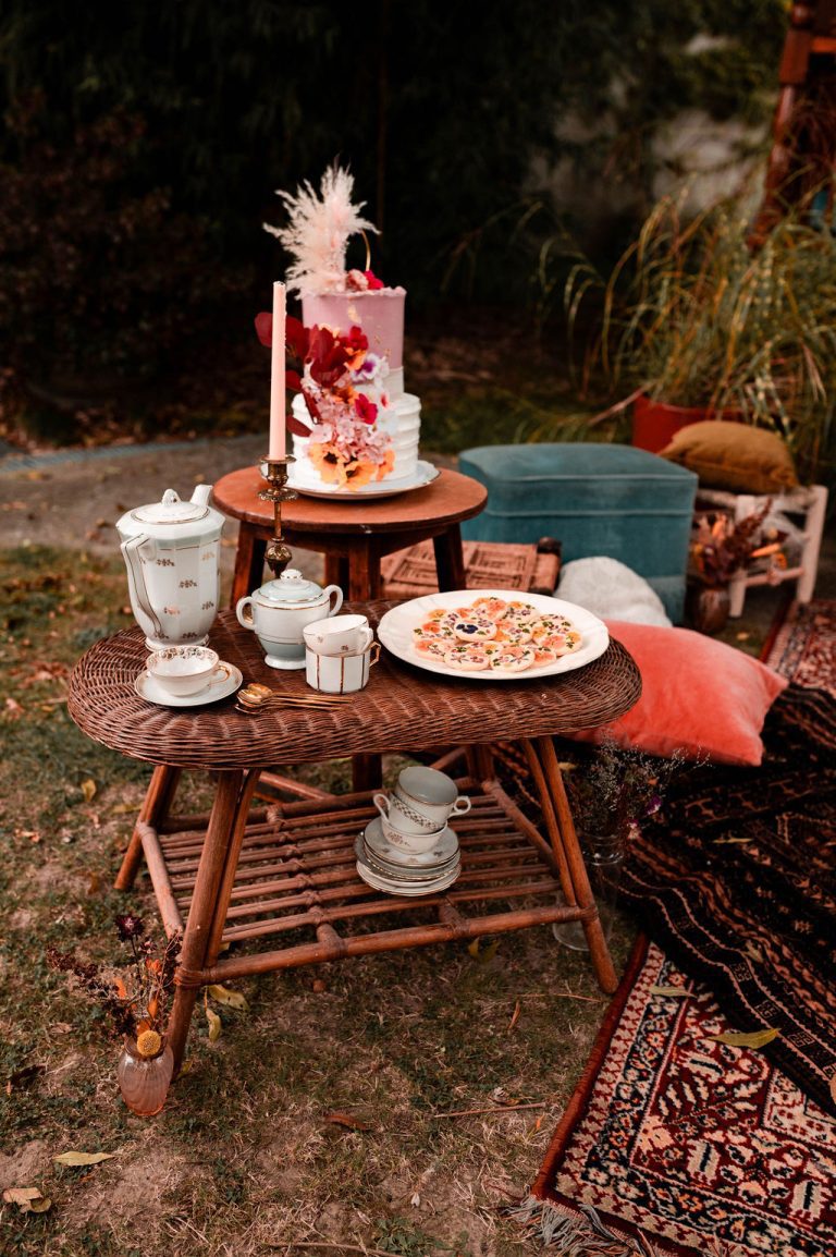 Table de goûter bohème avec gâteau, thé, et biscuits dans un cadre extérieur.
