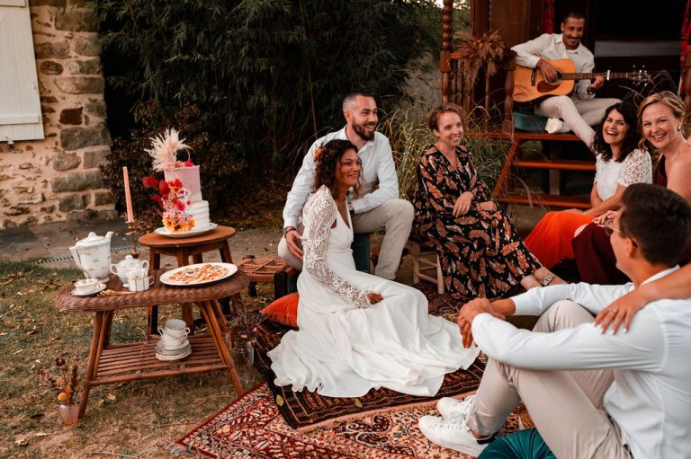 Mariés et invités partageant un moment convivial autour d'une table garnie, sous l'animation d'un guitariste.