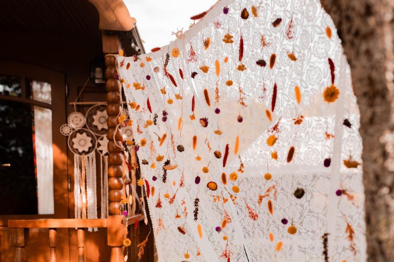 Rideau en dentelle blanche orné de fleurs et feuilles séchées avec attrape-rêves en arrière-plan.