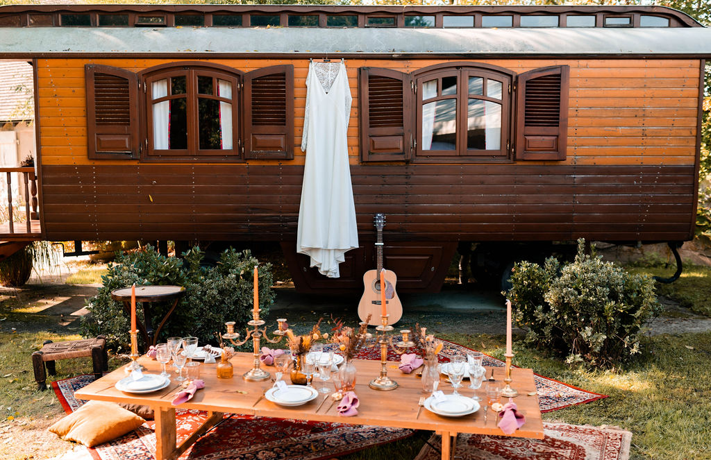 obe de mariée suspendue à l'extérieur d'une roulotte bohème avec une table dressée en premier plan.