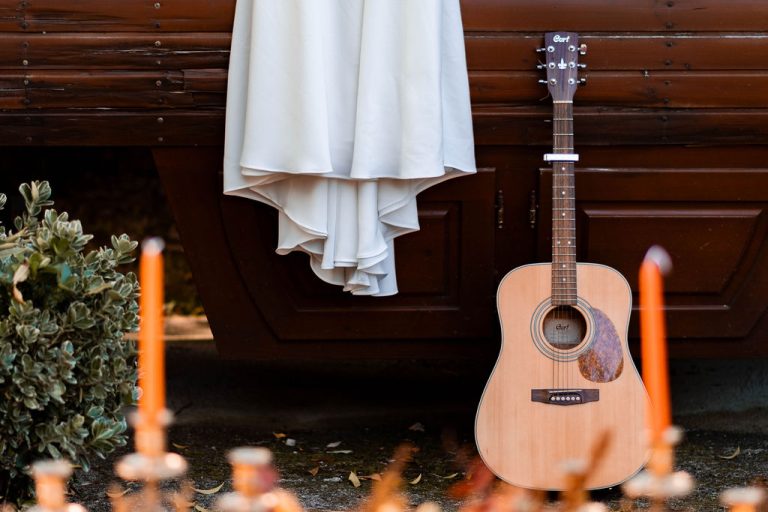 Robe de mariée blanche suspendue à côté d'une guitare accoudée à une roulotte.