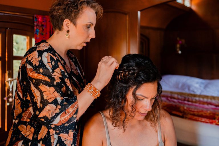 Coiffeuse arrangeant les cheveux de la mariée dans une roulotte colorée.