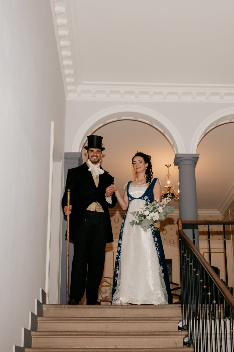 Les mariés descendent ensemble l'escalier, main dans la main, dans une élégante demeure, prêts à célébrer leur amour.