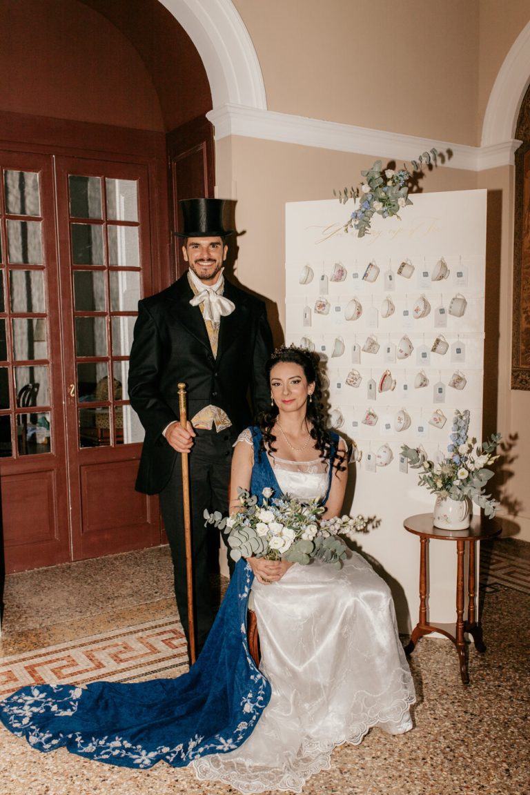 Couple marié posant devant un mur décoratif de tasses à thé, soulignant un thème de mariage élégant et unique.