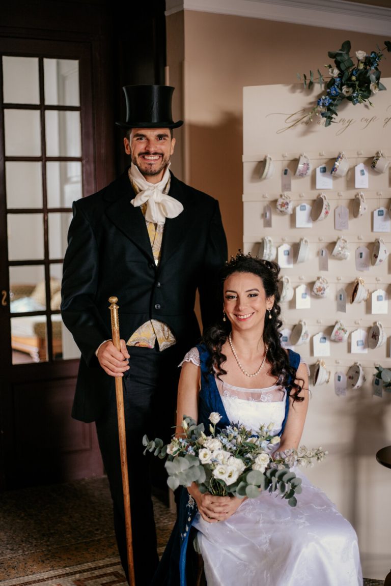 Mariés posant joyeusement devant un panneau de mariage, le marié avec un haut-de-forme et une canne.