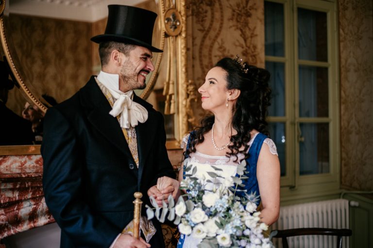 Couple marié en tenue d'inspiration Bridgerton se tenant la main devant un décor naturel romantique.