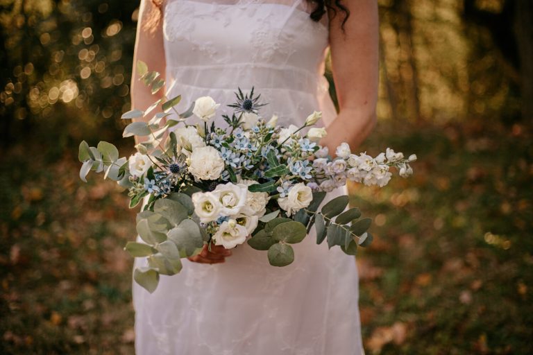 Mariée tenant un bouquet de fleurs blanches et bleues dans un décor forestier