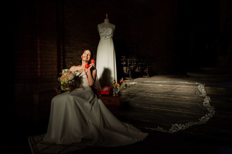Mariée souriante parlant au téléphone vintage assise près d'une robe de mariée.